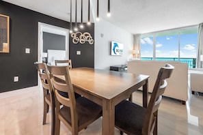 A modern dining area with a wooden table and chairs, a white door, a wall-mounted artwork, and a view of the ocean.