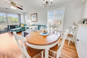 Un coin repas avec une table en bois, des chaises blanches et un ventilateur de plafond.