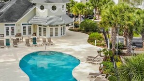 A pool with lounge chairs, a building with a distinctive curved roof, and palm trees. - NEW! Large 2BR| River Oaks Golf | Pools | Hot Tubs (Myrtle Beach)
