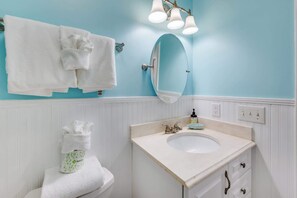 Une salle de bain avec un meuble-lavabo blanc, un évier, un miroir et un porte-serviettes.