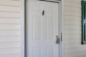 Une porte blanche avec une petite plaque au-dessus, un interphone et une fenêtre à cadre vert sur la droite.
