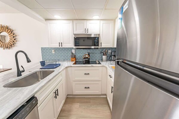 A modern kitchen with white cabinets, a stainless steel refrigerator, a microwave, and a sink with a dish rack.