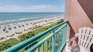 A balcony with a view of a beach with umbrellas and people. - New 1BR Direct Oceanfront  Sandcastle South, Pools (Myrtle Beach)