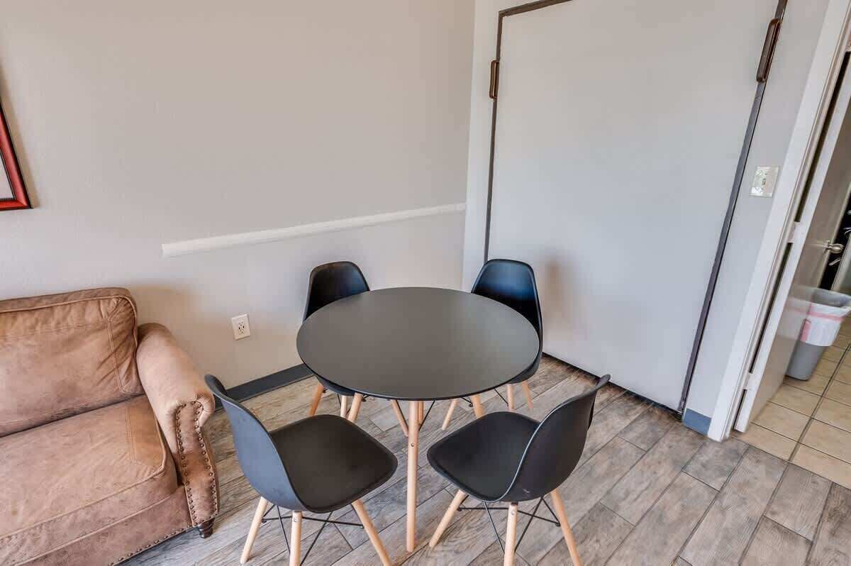 Una habitación pequeña con una mesa redonda y cuatro sillas, un sofá marrón y una puerta blanca.