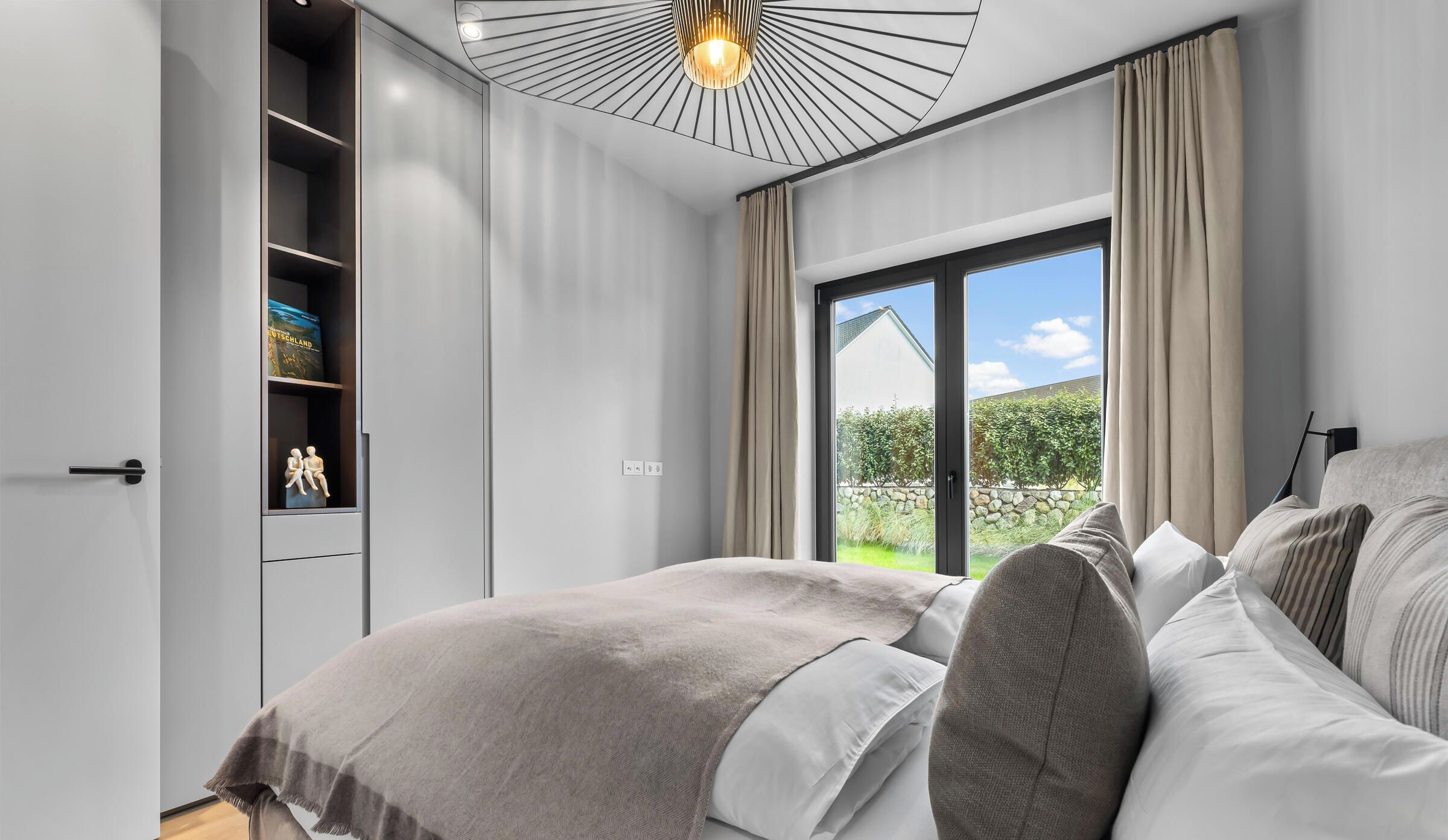 Una camera da letto moderna con un letto grande, un armadio e vista su un giardino tramite una porta scorrevole.