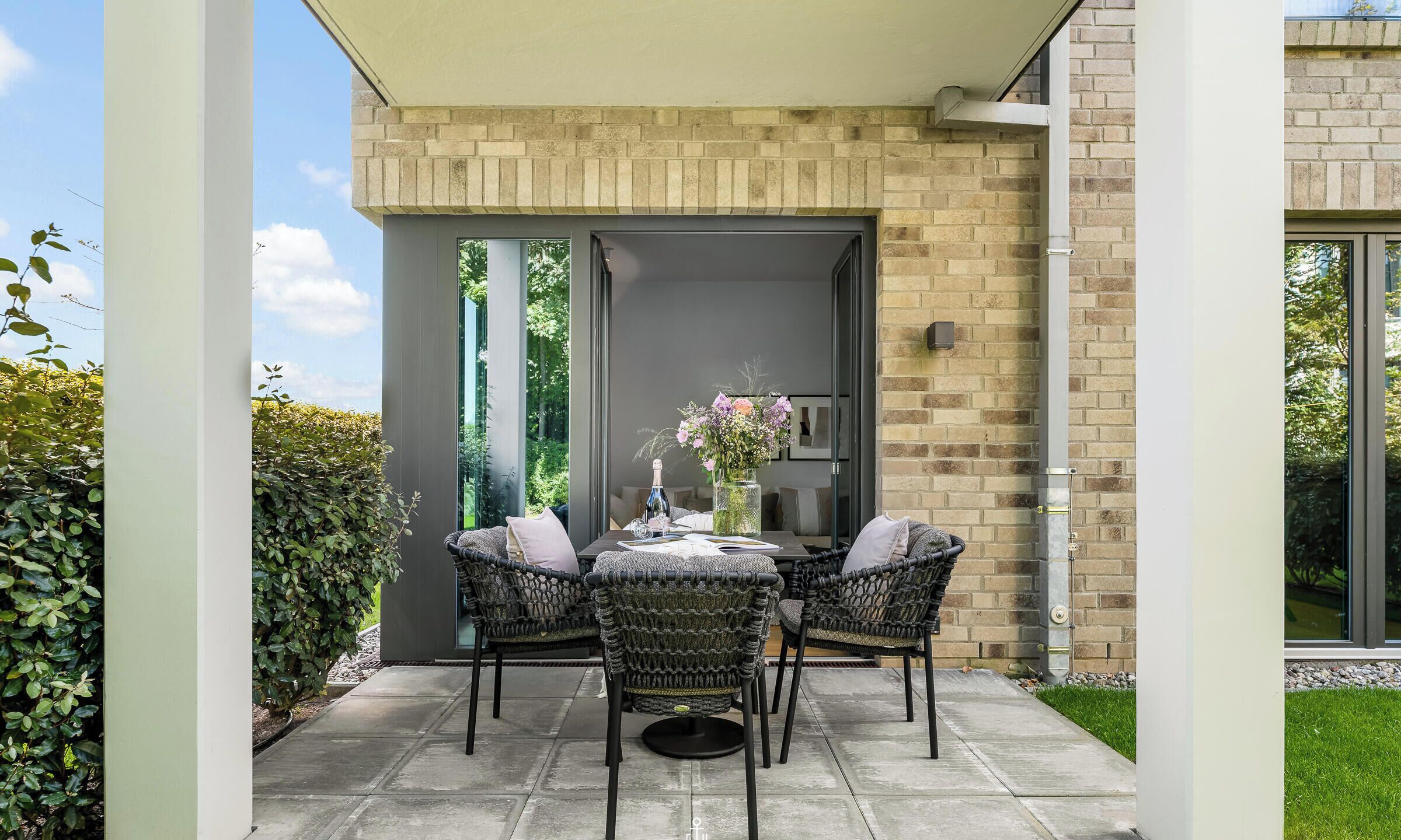 An outdoor patio with a table and chairs, a vase with flowers, and a brick wall.