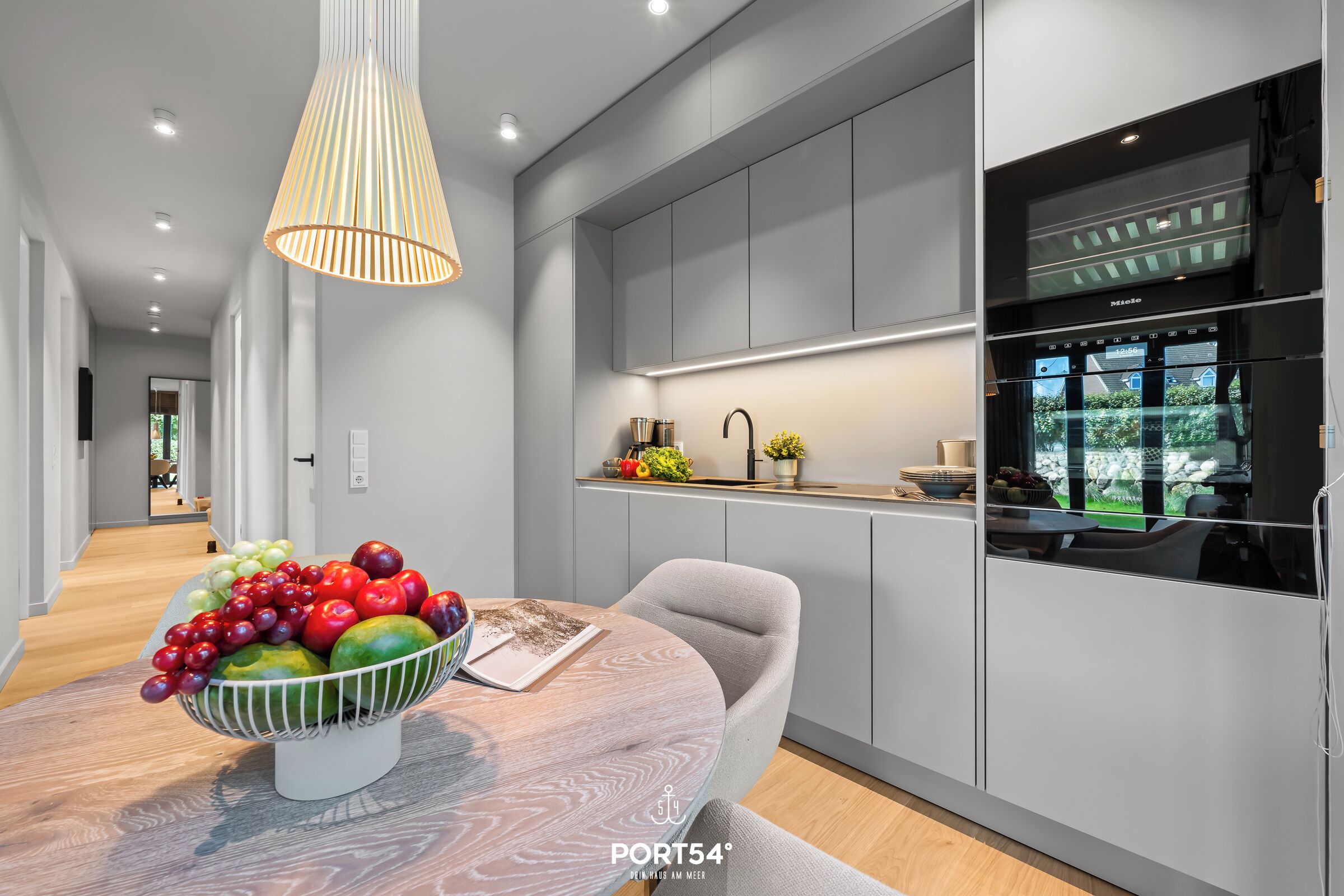 Una cocina moderna con armarios grises, una campana extractora de acero inoxidable y un frutero en la isla.
