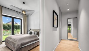 A modern bedroom with a large bed, a ceiling light fixture, and a view of the outdoors.