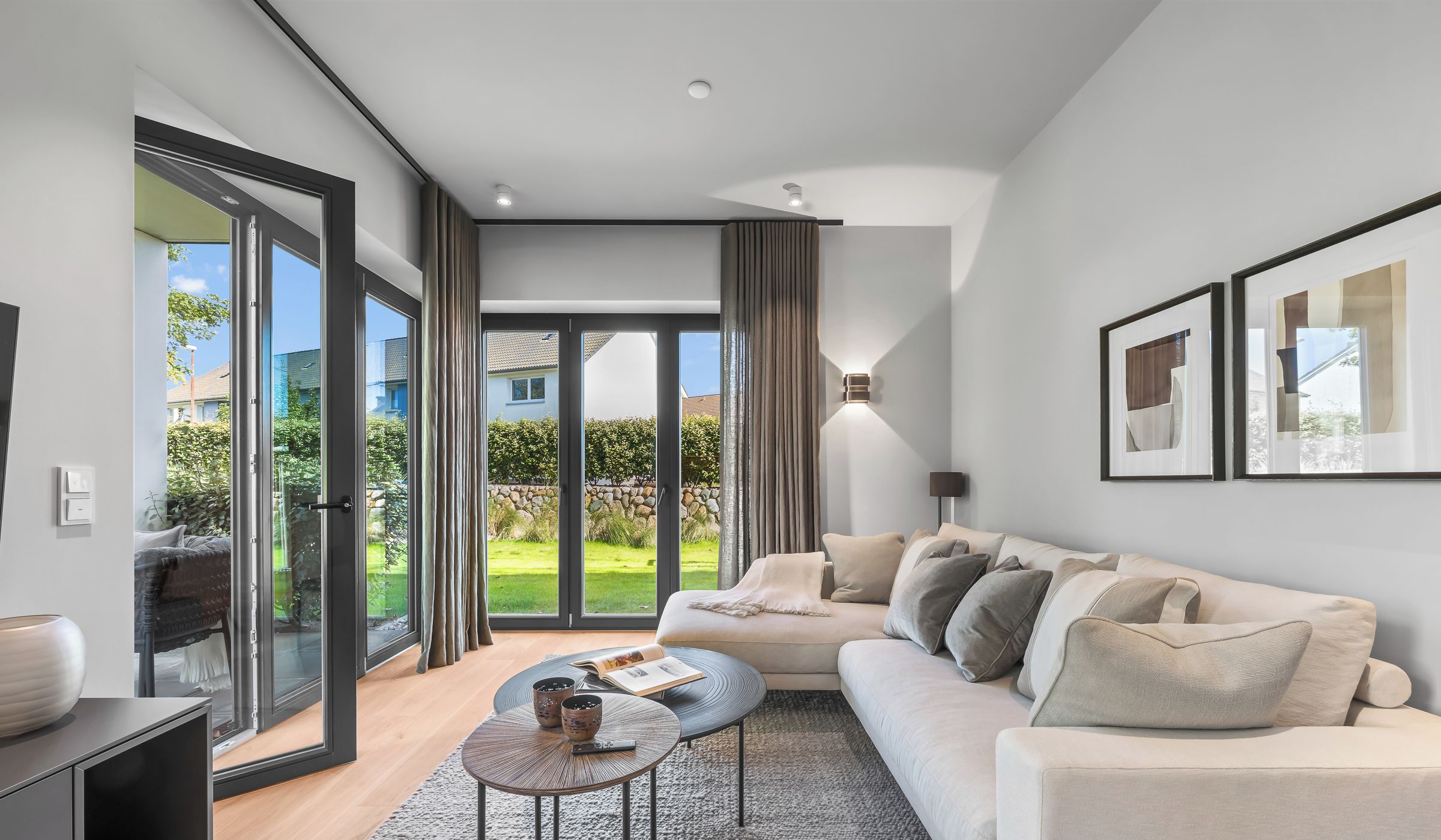 Een moderne woonkamer met een bank, salontafel en uitzicht op een tuin door grote glazen deuren.