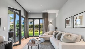 Un salon moderne avec un canapé, une table basse et une vue sur un jardin, visible à travers de grandes portes vitrées.