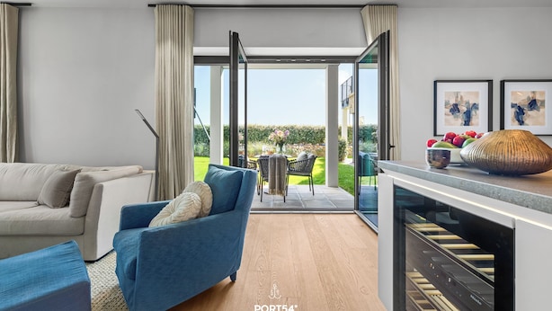 Un salon moderne avec un canapé, un fauteuil bleu et un coin cuisine doté d’un four encastré.