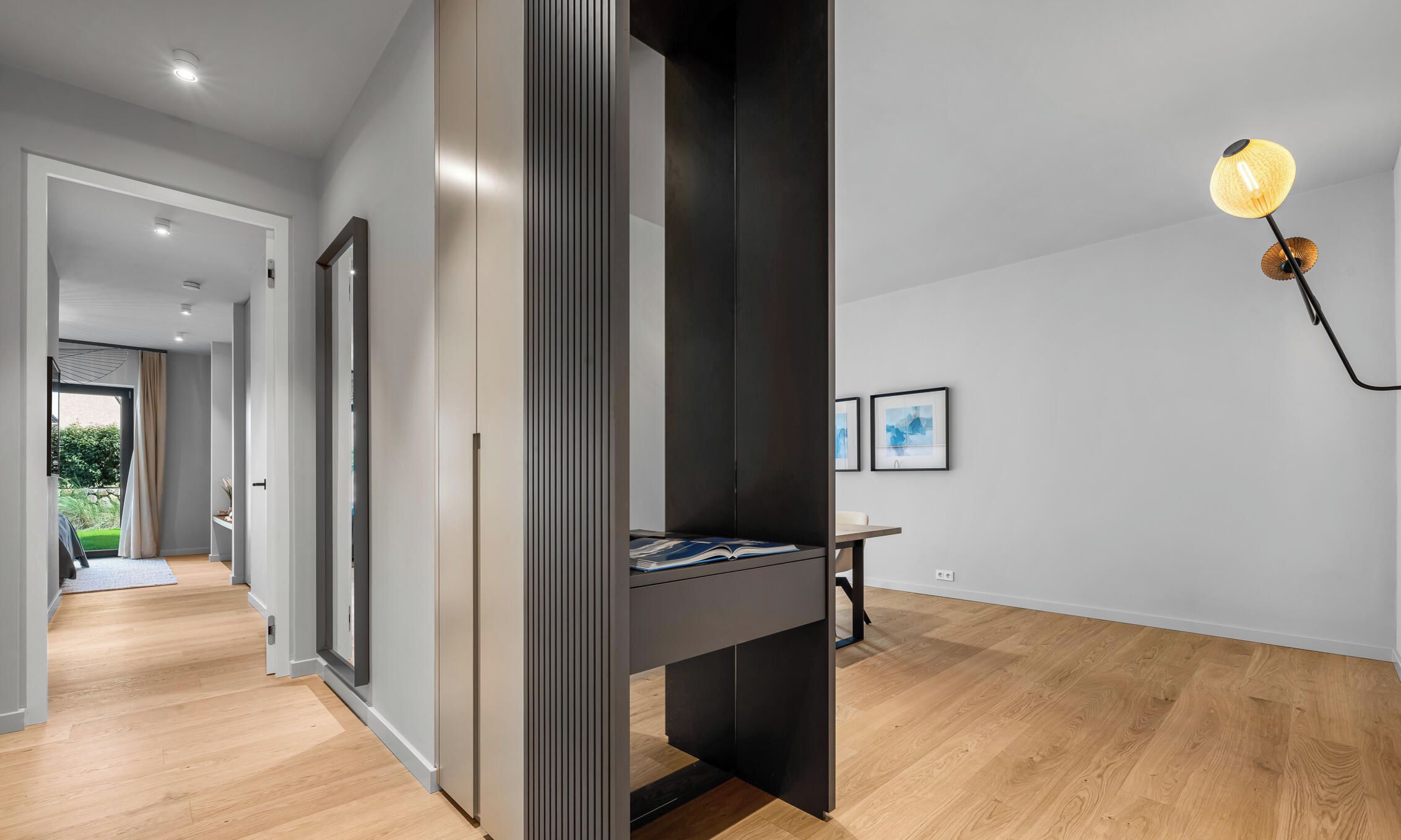 Een modern interieur met een hal die leidt naar een kamer met een donkere accentmuur en een bureau met een lamp.