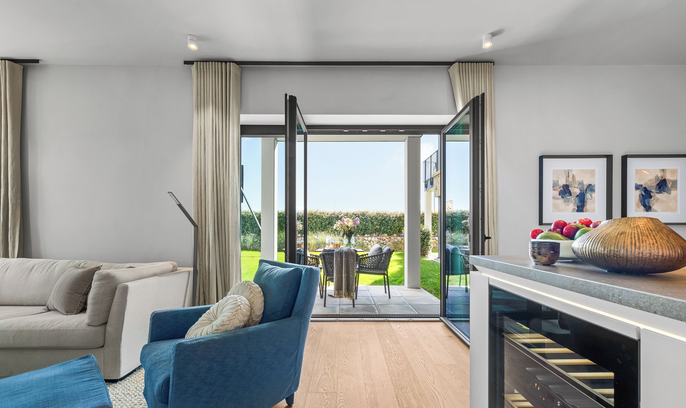 A modern living room with a sofa, a blue armchair, and a kitchen area with a built-in oven.