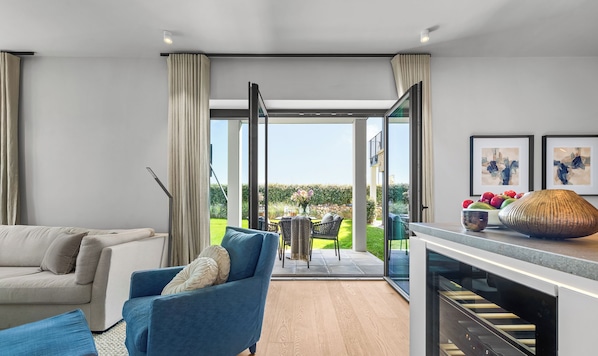 Una sala de estar moderna con un sofá, un sillón azul y una cocina con horno empotrado.