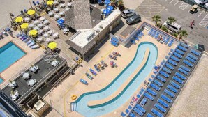 Et poolområde med liggestole og parasoller, en separat pool samt en bygning med tag.