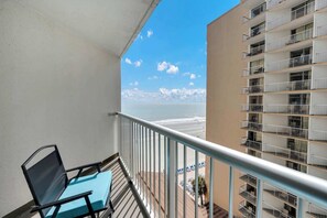 Un balcon avec vue sur la plage et l’océan, une chaise et une rambarde.