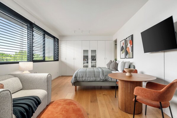 Une chambre moderne comprenant un lit, un coin salon avec une table et des chaises, un téléviseur et une armoire.