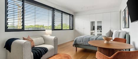 A modern bedroom with a large window, a bed, a sofa, and a dining area.