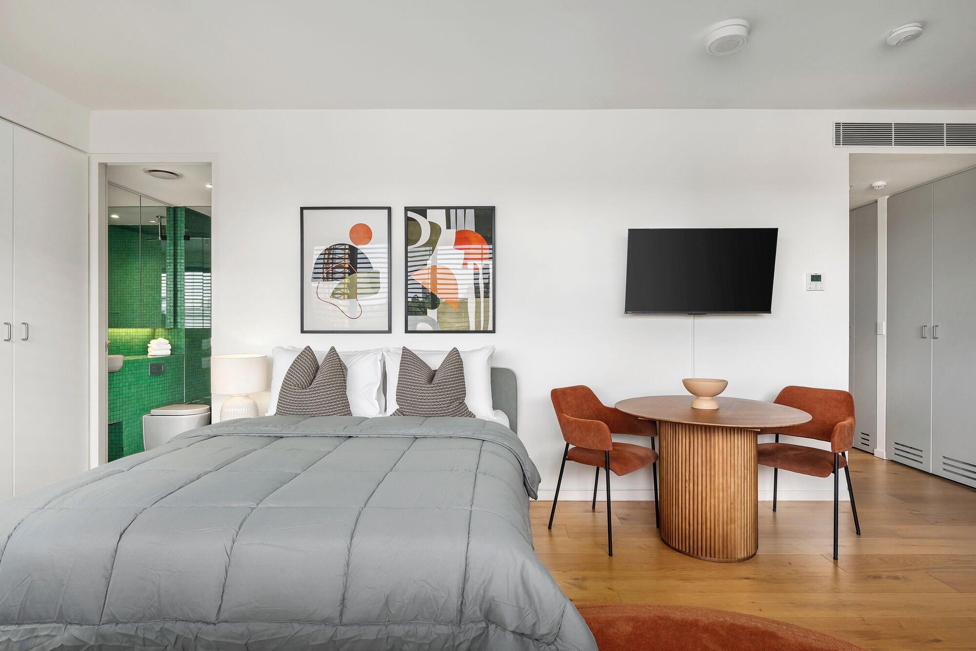 A modern bedroom with a bed, a TV, and a dining area with chairs.