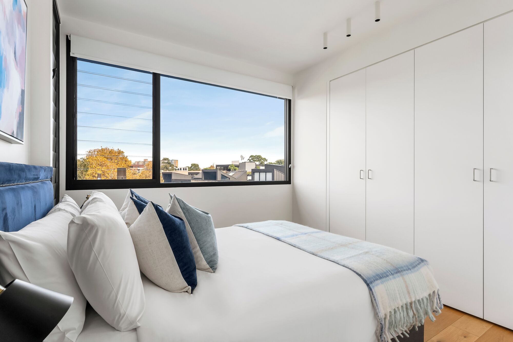 A bedroom with a bed, a window with a city view, and a wardrobe.