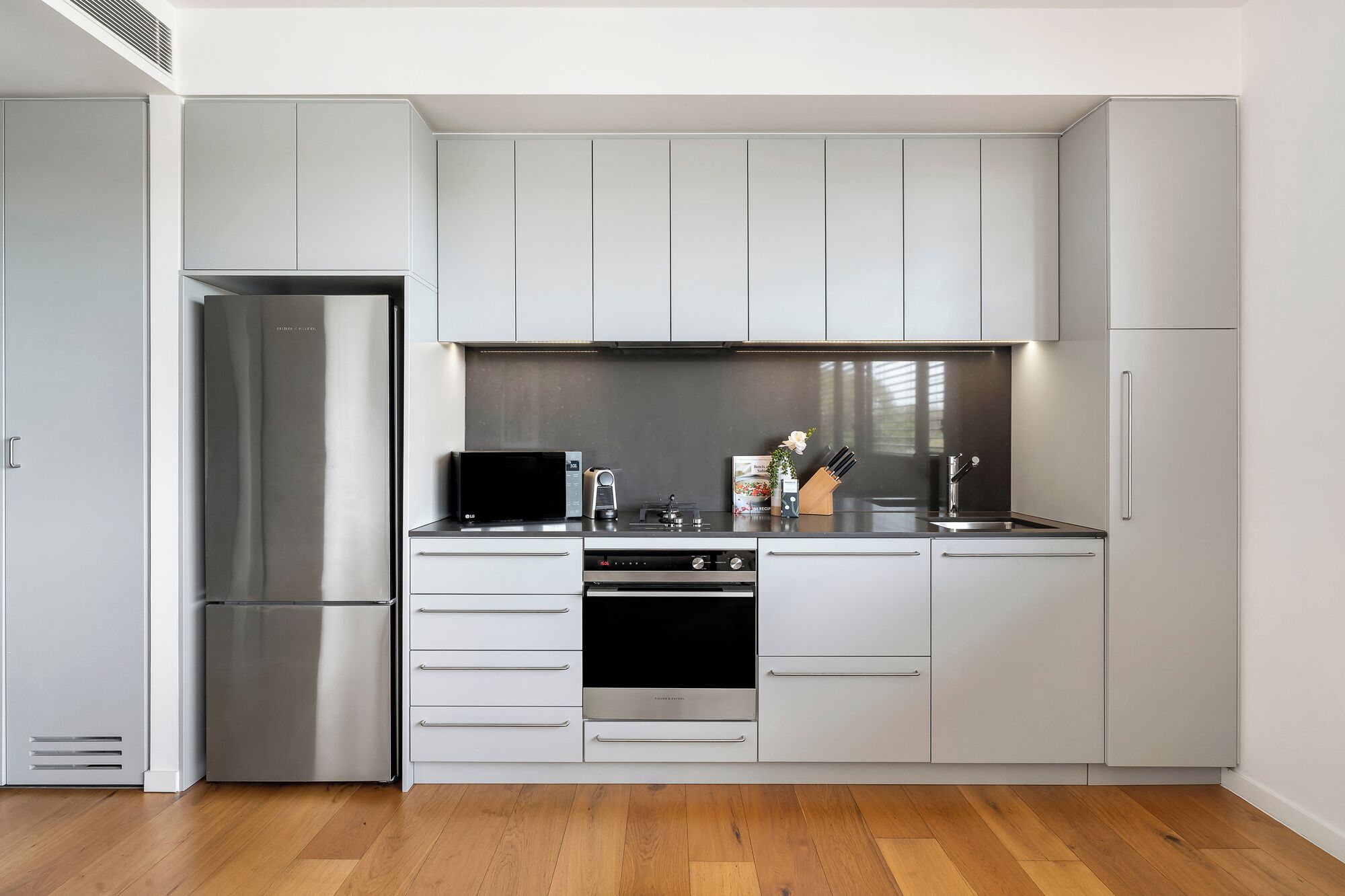 Une cuisine moderne avec des meubles gris, des appareils en acier inoxydable et un plancher en bois.