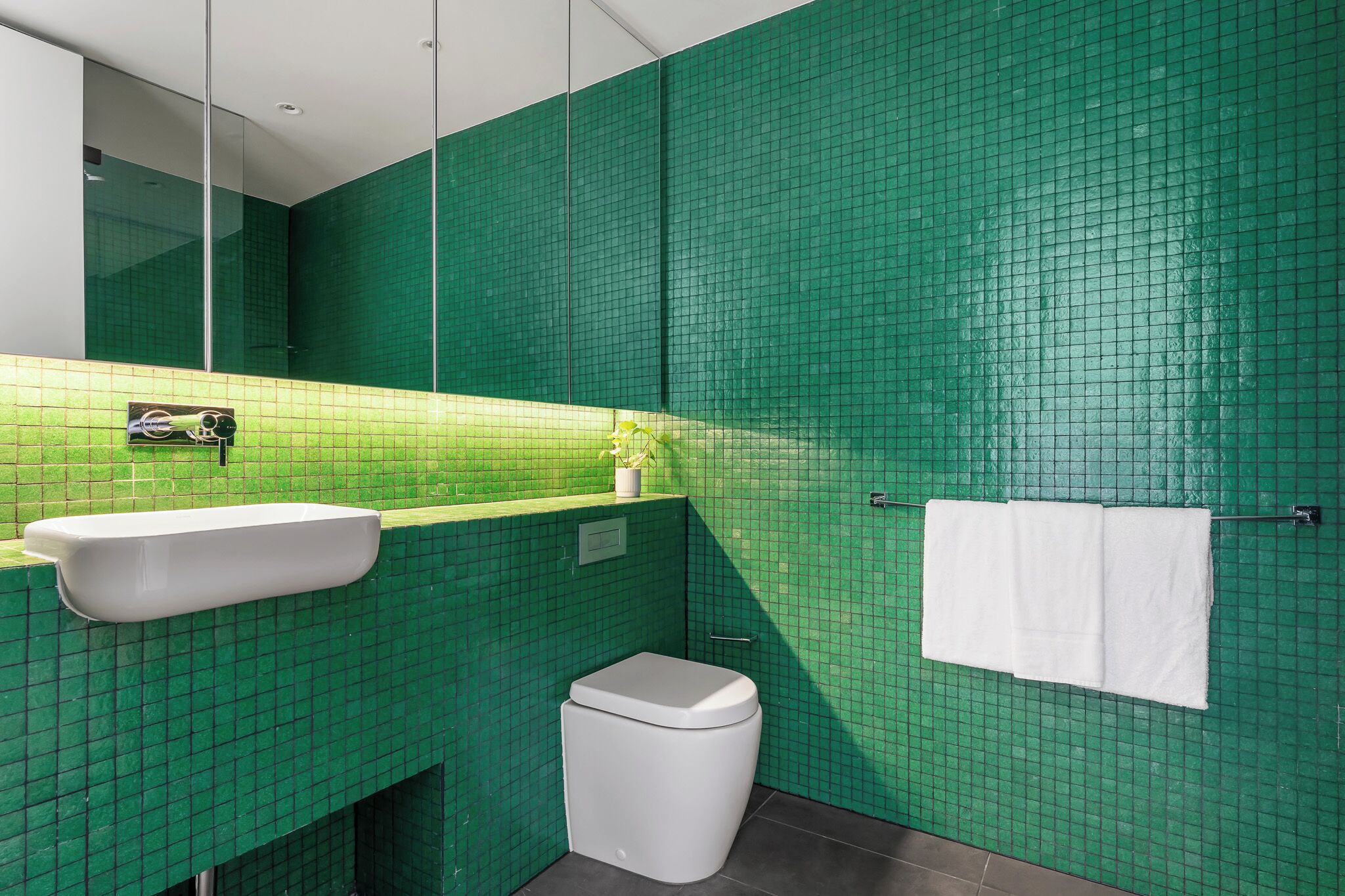 Un baño con paredes de azulejos verdes, un lavabo blanco y un inodoro blanco.