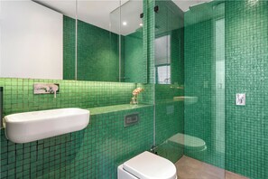 Un baño con mosaicos verdes, un lavamanos blanco y un inodoro.