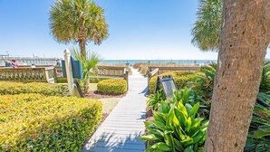A wooden pathway leading to a beach with palm trees and a fence. - Direct Ocean Front, The Pavilion, Pools, Boardwalk (Myrtle Beach)