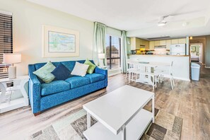 A living room with a blue sofa, white coffee table, and a dining area with a white table and chairs.
