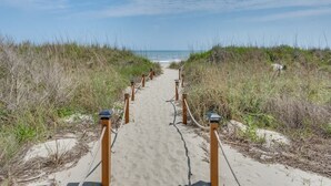 Un sendero arenoso que conduce a la playa, bordeado por hierba y postes de madera.