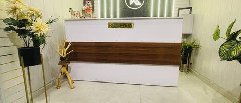 Una recepción con un logotipo, un cartel que indica los horarios de registro de entrada y salida, y un televisor montado en la pared.
