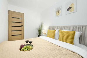 A bedroom with a bed, a bedside table with a lamp, a wall-mounted artwork, and a wooden door. - Lumina opposite the Palace of Culture and Science (Warszawa BIG)