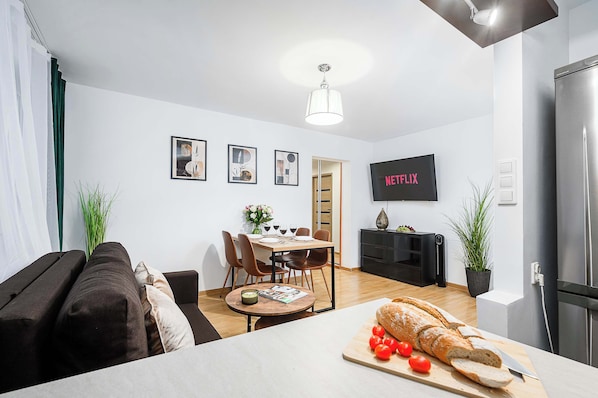 Een moderne woonkamer met een bank, eettafel en een televisie waarop 'NETFLIX' wordt afgespeeld.