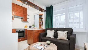 Een moderne keuken met houten kastjes, een inbouwoven en een zithoek met een donkere bank en een ronde tafel.