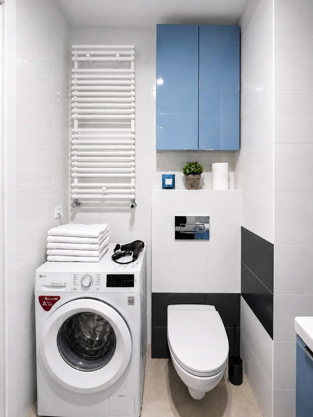 A compact laundry room with a front-loading washing machine, a toilet, and a blue cabinet above the sink.