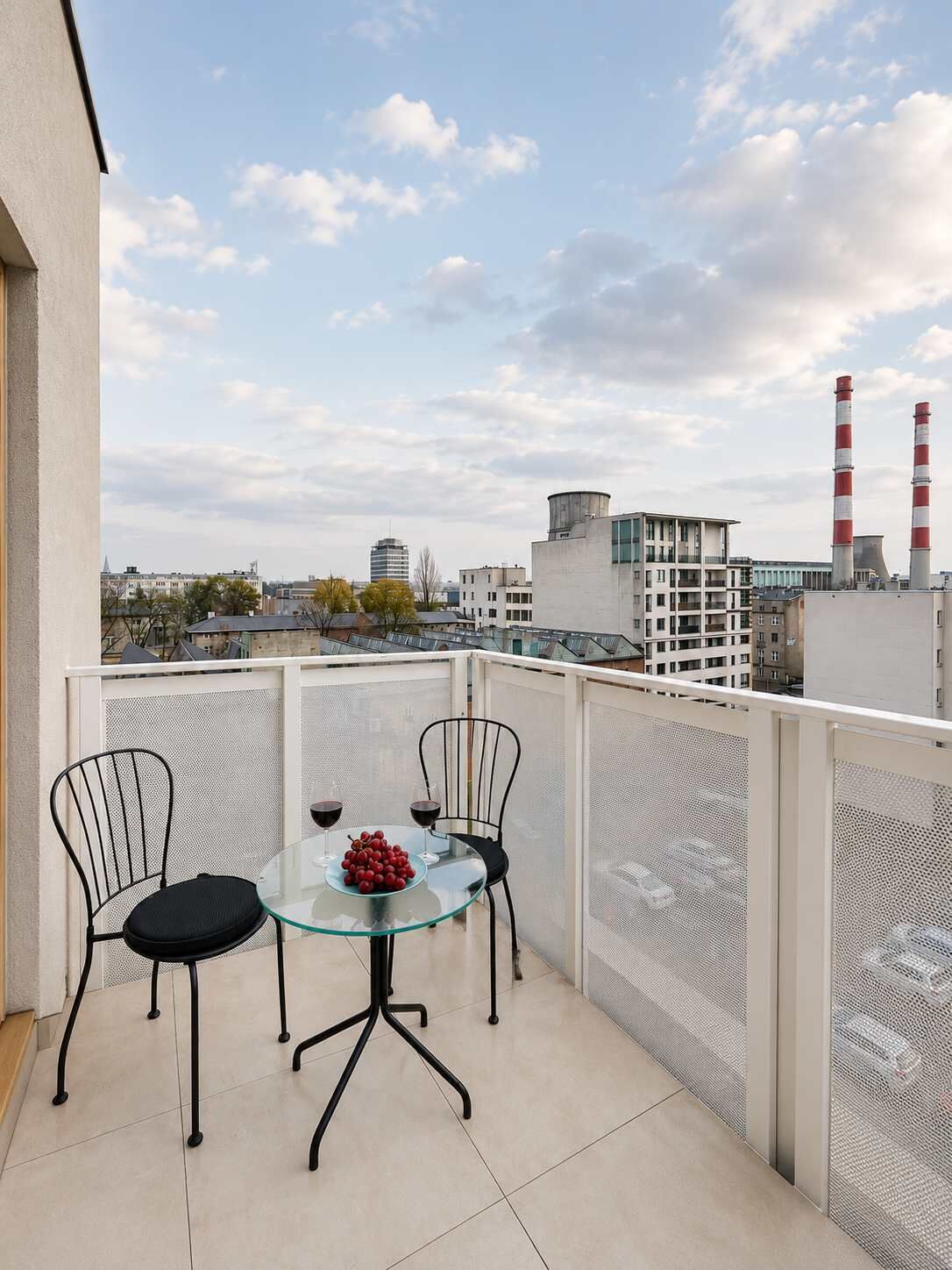 Un balcon avec une table en verre, deux chaises et un saladier rempli de fruits.