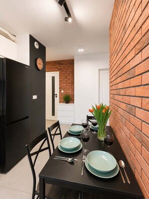 Une cuisine moderne avec un réfrigérateur noir, une table à manger dressée avec des assiettes, des verres et un vase de fleurs.