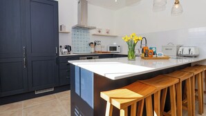 Una cocina moderna con armarios oscuros, una isla blanca, taburetes de madera, microondas, tostadora y un florero con flores amarillas.
