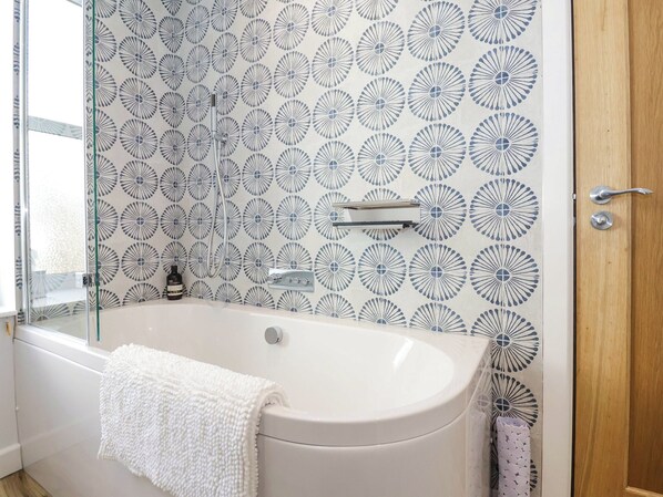 Un baño con una bañera independiente, cabina de ducha con mampara de vidrio y pared con diseño.