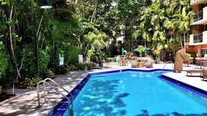 A swimming pool with a blue edge, surrounded by greenery and outdoor furniture.