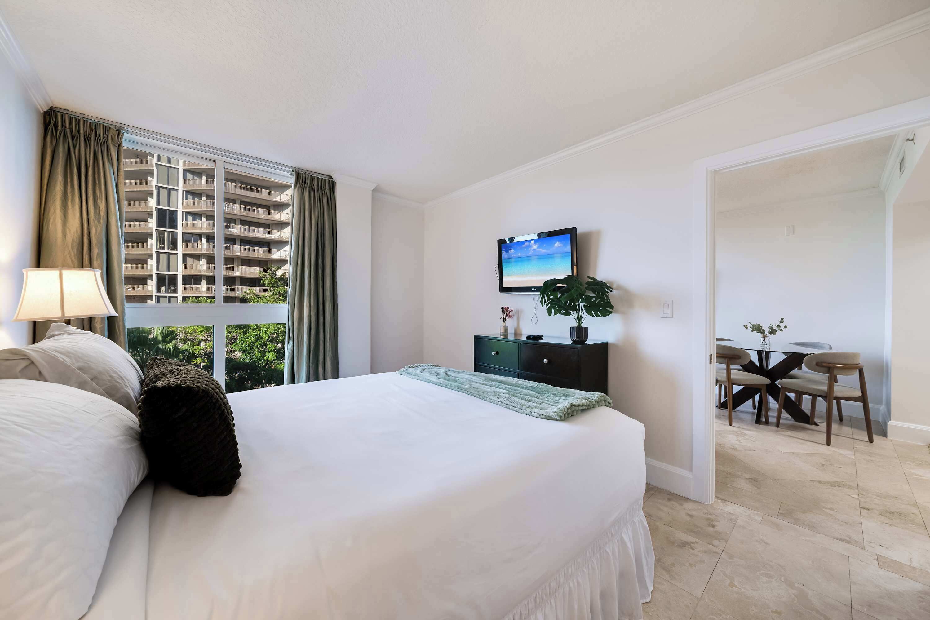 Ein Hotelzimmer mit Bett, Fernseher, Schreibtisch und Blick auf ein Gebäude.