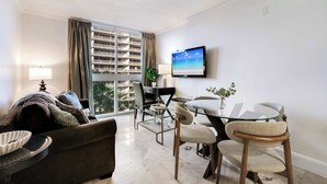 A modern living room with a sofa, a glass dining table, and a TV mounted on the wall.