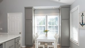 A kitchen with a white table, grey cabinets, and a window with blinds.