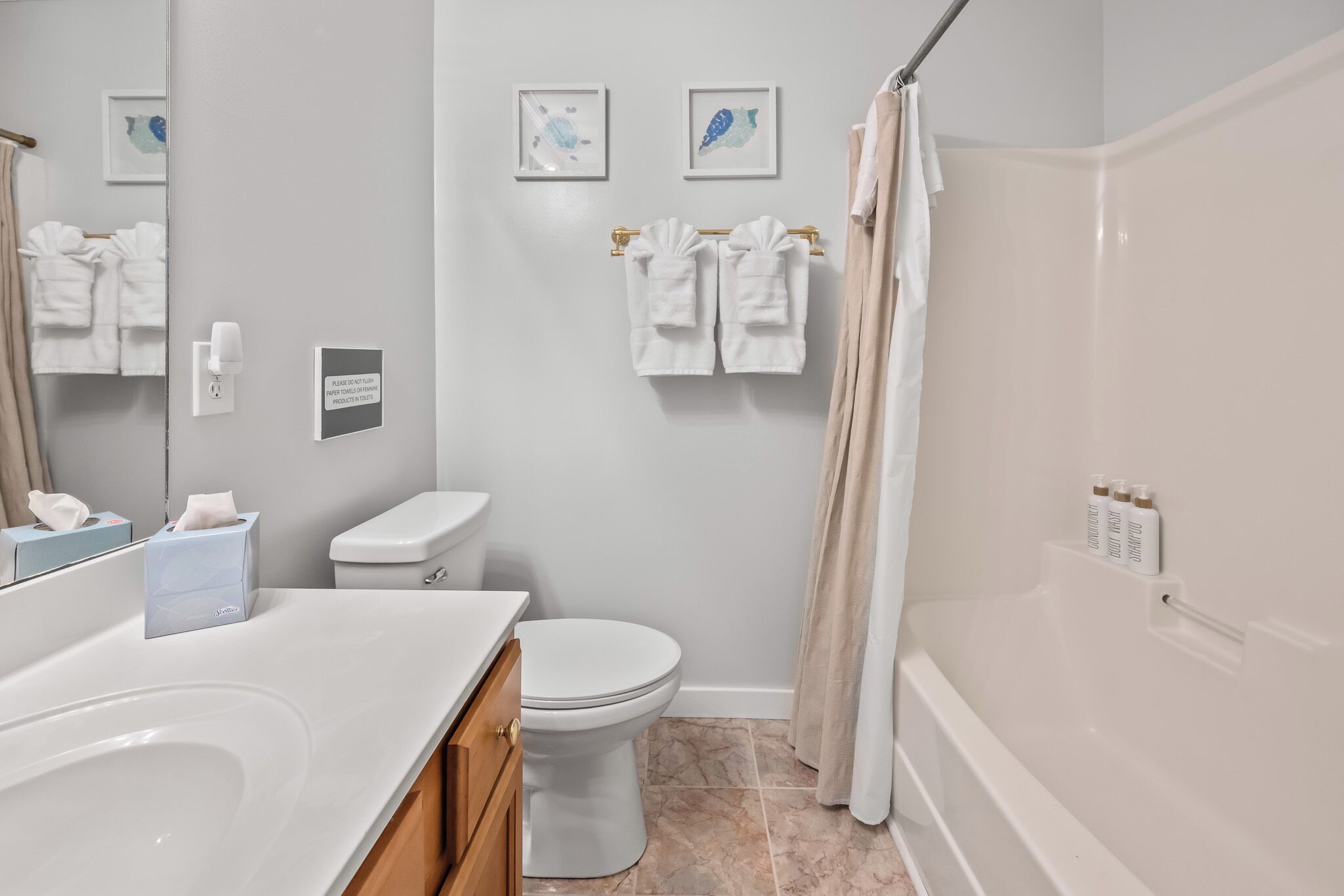 Een moderne badkamer met een wit toilet, een badkuip en een douchegordijn. Handdoeken hangen aan een rek en er is een handdroger aan de muur.