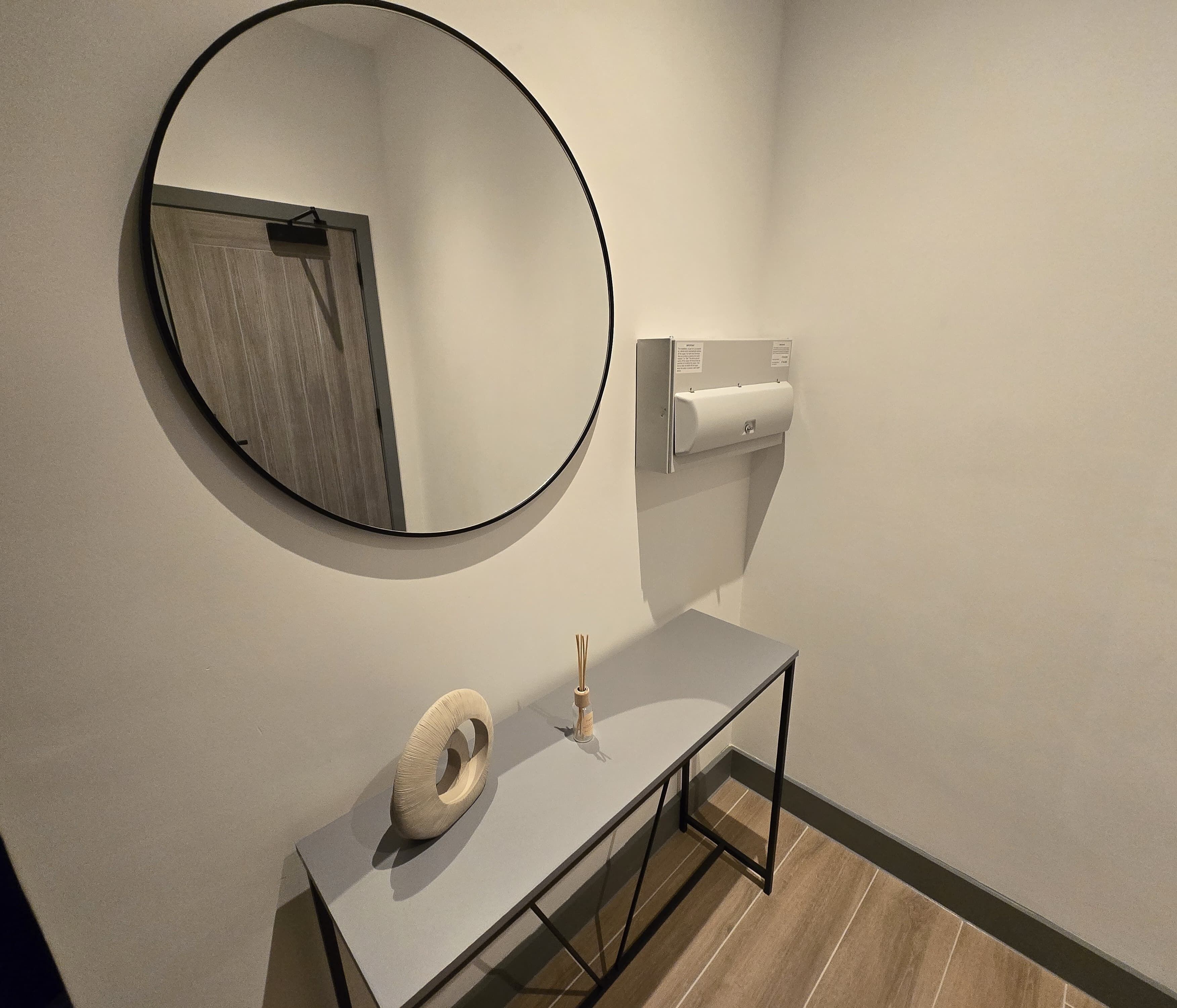 Une salle de bain avec un miroir rond, un porte-rouleau de papier toilette et des toilettes.