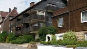 Un immeuble résidentiel à plusieurs étages, doté de balcons, d’un mur en pierre et d’un petit jardin.