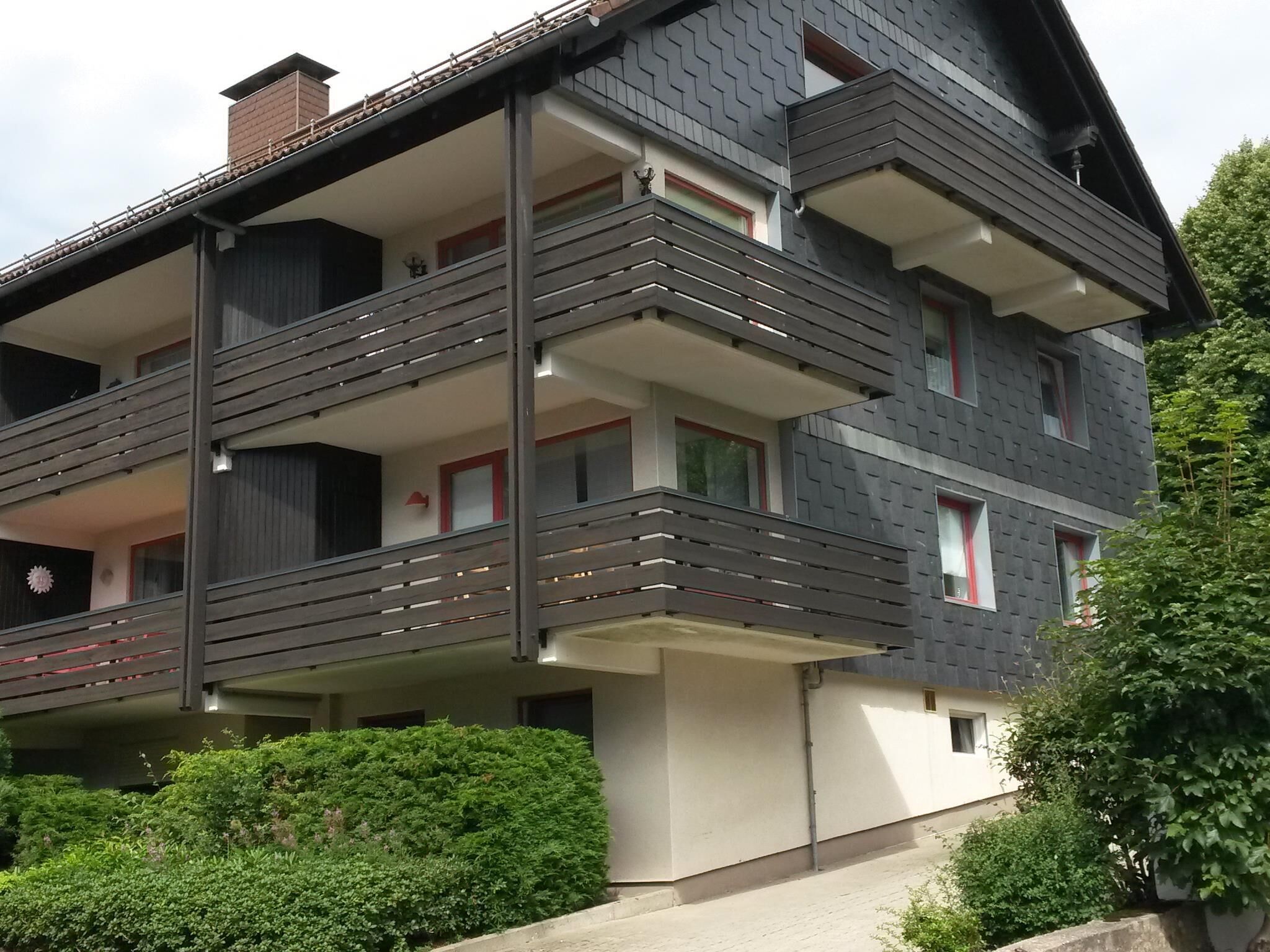 Ein mehrstöckiges Gebäude mit Balkonen, einem Schornstein und einem gepflegten Garten.