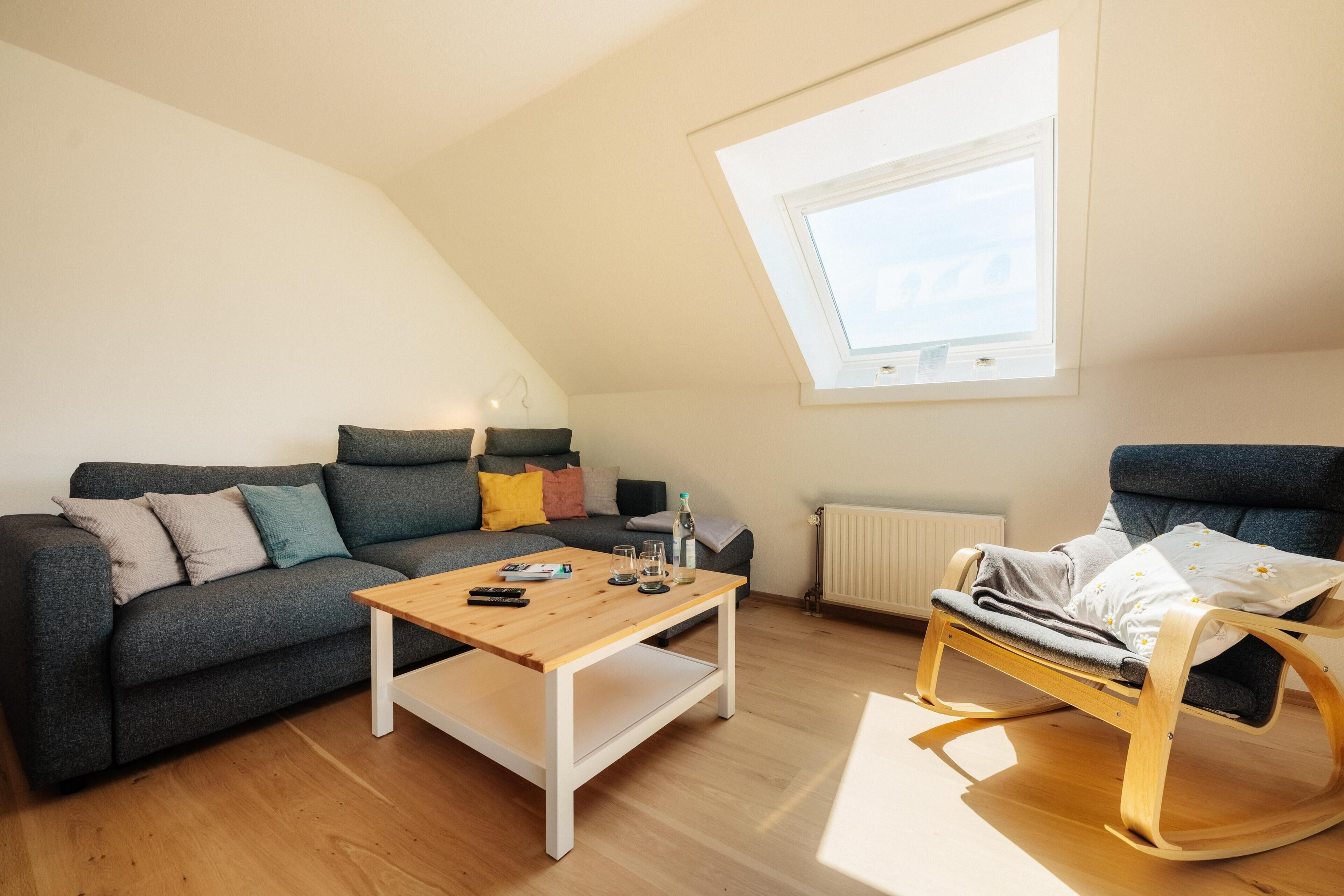 Ein gemütliches Wohnzimmer mit einer Couch, einem Holztisch, einem Schaukelstuhl und einem Oberlicht.