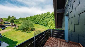 A balcony with a view of a green landscape and a building with a dark exterior.