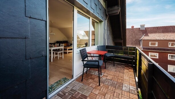 Un balcon avec une table et des chaises, un plancher en bois et une vue sur le ciel et les bâtiments.